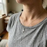Persona usando un collar con una pequeña cruz de plata sobre una camiseta casual.