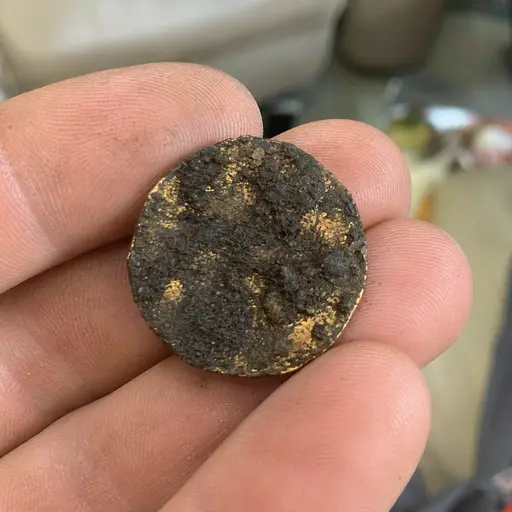 Mano sosteniendo una antigua moneda de oro puro cubierta de lodo y óxido.